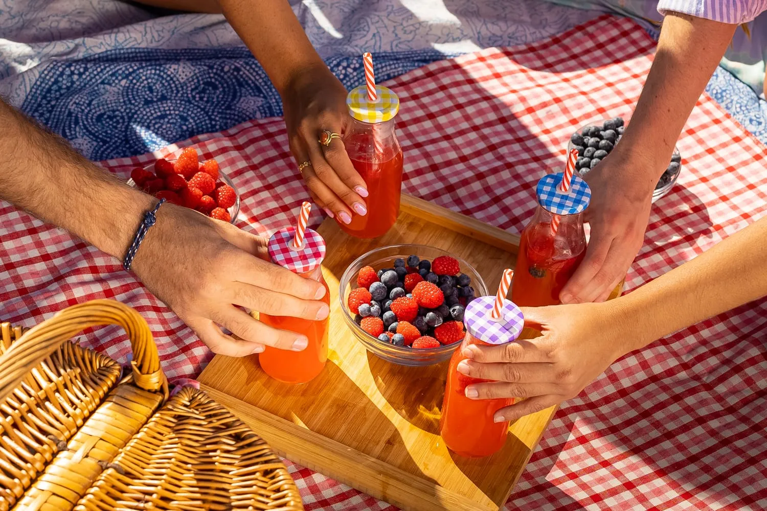 Manos cogiendo bebidas de frutos rojos junto a un bol de berries en un pícnic en la playa